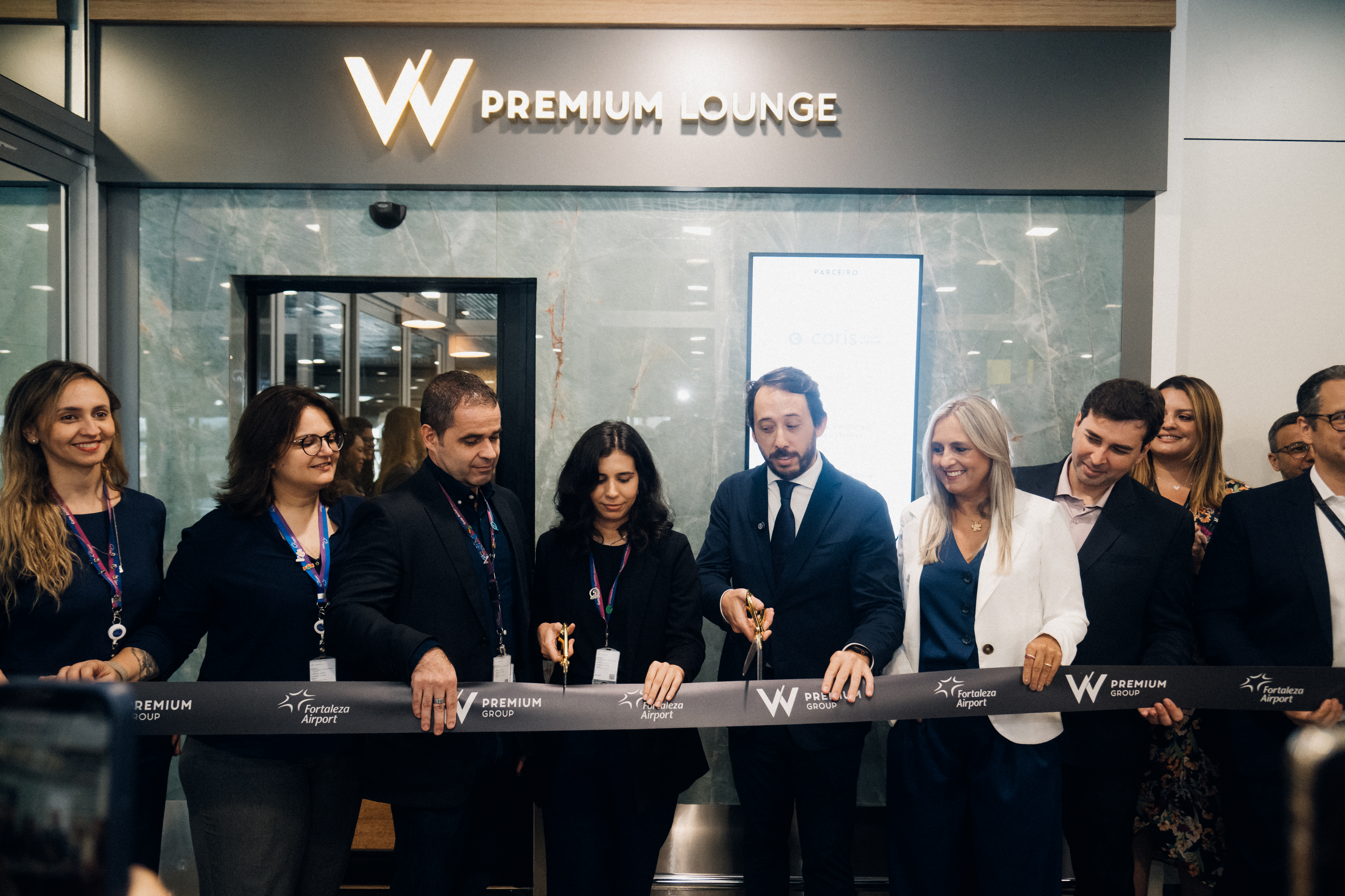 Cerimônia de inauguração do W Premium Lounge, com executivos cortando uma fita preta diante de um painel de marca com letreiro luminoso.
